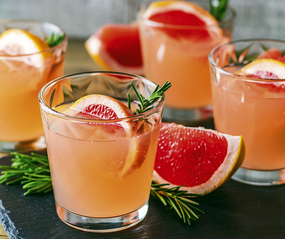 Fresh pink alcoholic cocktail with grapefruit, ice and rosemary, drink glass on a black stone board, old rustic style, selective focus, shallow depth of the field.