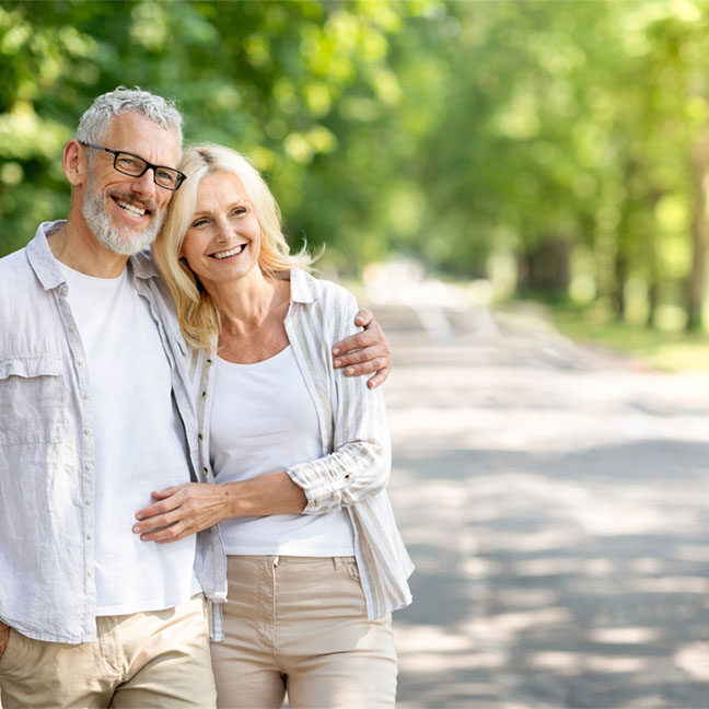 Beautiful mature spouses hugging outdoors while walking in summer park, happy senior couple embracing and looking away, older husband and wife enjoying time together, having romantic date outside