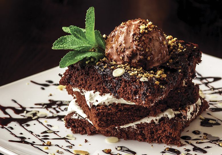 Chocolate brownie cake with a scoop of ice cream with a mint leaf on a white plate
