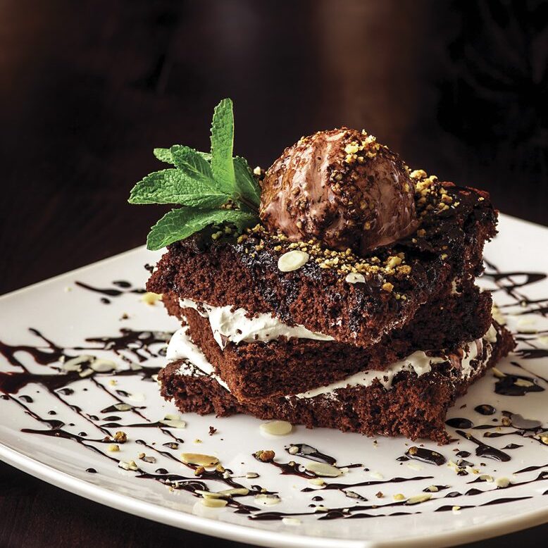 Chocolate brownie cake with a scoop of ice cream with a mint leaf on a white plate